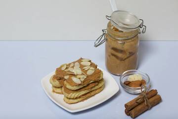 Eclairs cake smeared with cinnamon cream. Nearby ingredients for cooking. On a white surface.