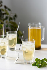 Cold refreshing green tea with ice and mint, tea jug and glasses on white wooden background
