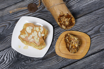Eclairs cake smeared with cinnamon cream. Energy bar made from dried fruits, nuts and seeds. On black pine boards.