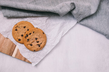 chocolate chip cookies on light background with linen napkins, a wooden cutting board, and baking paper. Yummy food background. Dessert image.