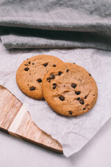 chocolate chip cookies on light background with linen napkins, a wooden cutting board, and baking paper. Yummy food background. Dessert image.