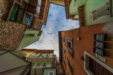 Rovereto, Italy street blue sky in small historic medieval town village in Trento looking up low angle vertical view during sunny summer day multicolored colorful painted walls and balcony