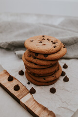 chocolate chip cookies on light background with linen napkins, a wooden cutting board, and baking paper. Yummy food background. Dessert image.