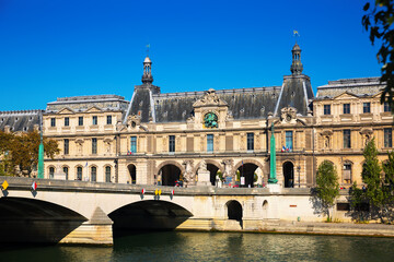 Obraz na płótnie Canvas View of Pont du Carrousel across Seine river leading to arched entrance to Louvre palace courtyard, Paris, France..