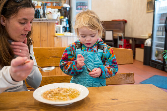 Cute blonde girl eating beef noodle soup in a restaurant with her mother.