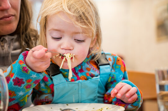 Cute blonde girl eating beef noodle soup in a restaurant with her mother.