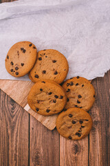 Chocolate chip cookies with baking paper on wooden background. Freshly baked sweets.
