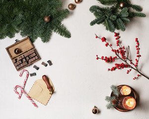 The space for the text is surrounded by Christmas decorations: fir branches, Christmas decorations, a wooden lettering stamp and a craft envelope. Candles and Christmas branch with red berries.