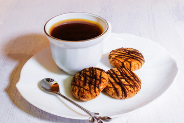 Hot coffee with oatmeal cookies with chocolate on a white plate.