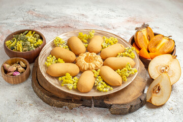 cookies on wooden platter and dry flowers and palm and pear on white marble ground