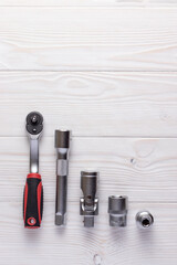 Ratchet wrench with replaceable nozzles on white wooden background.