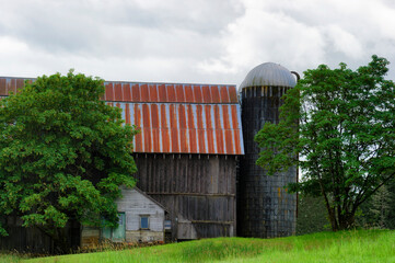 Fototapeta na wymiar Barn and silo on a hillside under cloudy sky