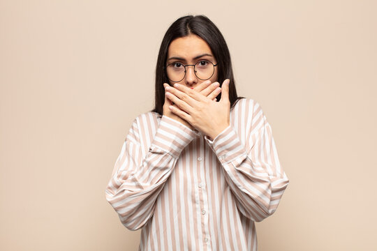 young hispanic woman covering mouth with hands with a shocked, surprised expression, keeping a secret or saying oops