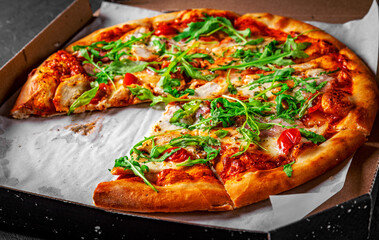 Pizza with chicken, bacon, cheese, tomato and arugula in paper box. Italian pizza on Dark grey black slate background