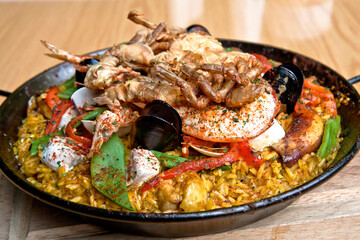 Paella with prawns, mussels, fish and octopus served in a frying pan on a wooden table