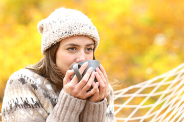 Satisfied woman drinking coffee in a hammock in autumn