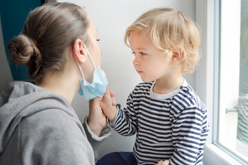 Obraz na płótnie Canvas Child in home quarantine taking the medical mask off his mothers face during coronavirus COVID-2019 and flu lock down. Selective focus