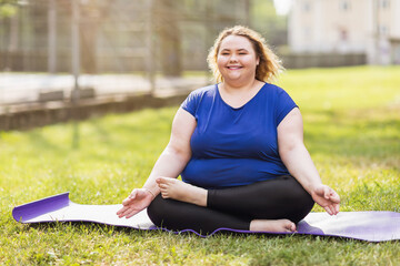 A happy young woman of size plus is engaged in yoga in the park in a warm sunny evening