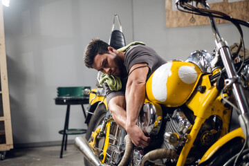 A young sports motorcycle repairman in a garage or workshop is working on a yellow bike