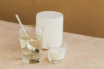Glass with collagen dissolved in water and collagen protein powder on a light beige table. Healthy lifestyle concept.