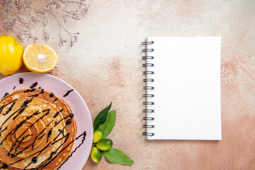 Fototapeta na wymiar Delicious classic pancakes decorated with chocolate syrop and fruits next to notebook