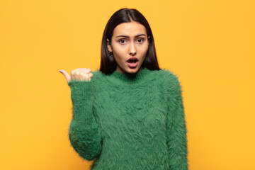 young hispanic woman looking astonished in disbelief, pointing at object on the side and saying...