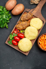 Close up view of tasty cutlets with vegetables and a bunch of green on dark table