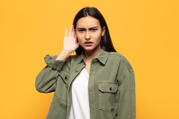 young hispanic woman looking serious and curious, listening, trying to hear a secret conversation...