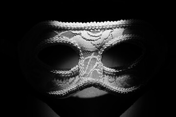 White festive carnival mask in the shadow of a point light on a black background.