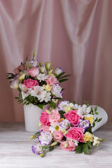 two bouquets of roses, daisies, lisianthus, chrysanthemums, unopened buds, one lying on a plank table and a background of silk fabric with pleats.