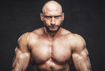 Fototapeta na wymiar Portrait of a muscular athlete with bearded and serious face and hairless head posing in dark background looking at camera.