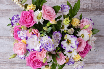 close-up flat lay bouquet of roses, daisies, lisianthus, chrysanthemums, unopened buds on a wooden shabby board background.