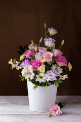 a luxurious bouquet of roses, daisies, chrysanthemums, unopened buds in a white round box, a sprig of lisianthus on a gray table and a background of burlap.