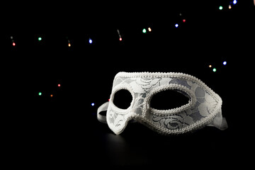 White festive carnival mask on a black background with multicolored garlands.