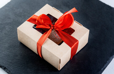 Christmas gift in a paper box on a black slate tied with a red ribbon.