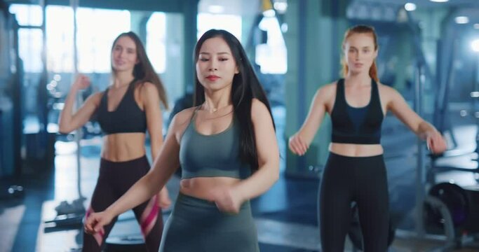 Diverse group of three amazing women doing cardio aerobics warming-up workout together in the gym. Workout session. Girl power. Athletic females.