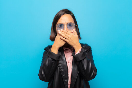 young hispanic woman covering mouth with hands with a shocked, surprised expression, keeping a secret or saying oops
