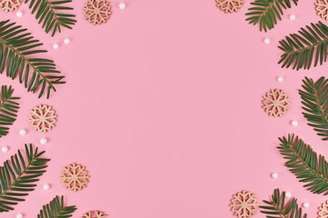 Seasonal taxus tree branches and snowball and snowflake ornaments forming border around pink background with empty copy space