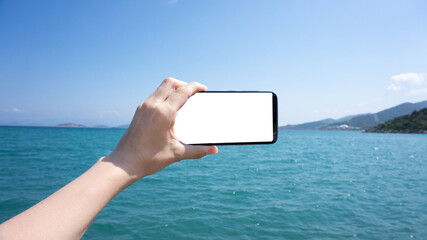 Horizontal smartphone. Tourist hand holding a black blank space screen smart phone while in vacation in the beach with view of the water blue landscape. Coast of Turkey, Aegean Sea