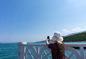 Woman tourist making a photo with her smartphone of the blue sky and water during a holiday vacation. Wearing a hat. Bodrum, Turkey, Aegean Mediterranean Sea