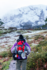 Unrecognizable hiker carrying a backpack and ascending a snowy mountain in winter. vertical stock image. camping utensils.