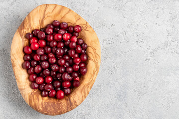 Ripe fresh cranberries in a wooden bowl on a gray table, copy space, top view, flat lay