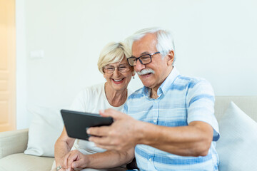 Fototapeta premium Senior couple using digital tablet at home. Grandparents using social media. Elderly couple together at home retirement concept using digital tablet