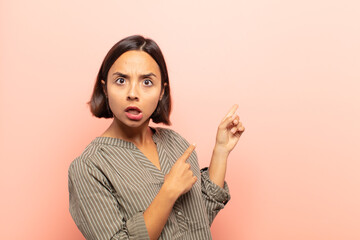 young hispanic woman feeling shocked and surprised, pointing to copy space on the side with amazed,...