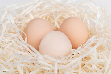 Raw brown and white eggs in nest made of staw shreded paper.