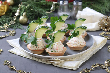 Tartlets with crab sticks, cream cheese and cucumber on a plate on grey background. Festive New Year snack. Closeup. © Anzhela