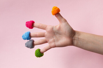 hello winter, female hand with fingers wearing warm colorful knitted hats isolated on pink