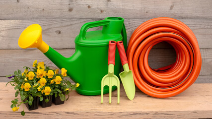 Green garden tools and watering hose stand on wooden background