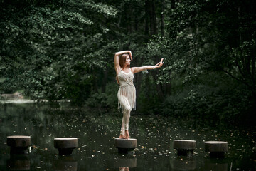 Beautiful young slender woman dancing on near pond and forest. Clothing of their eco-materials, macrame. The concept of natural products.