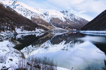 Lake in Trentino alto Adige, in Italy, during the winter period spectacular reflection on a frozen lake and a suggestive wooden Tibetan bridge.